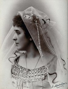 A woman posing in a photographic studio, wearing a bridal? dress and veil, in front of..., 1900-1910 Creator: Unknown.