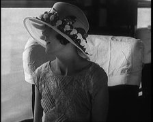 Female Civilian Wearing a Large Fashionable Hat Decorated with Flowers Seating at the Window...1920. Creator: British Pathe Ltd.