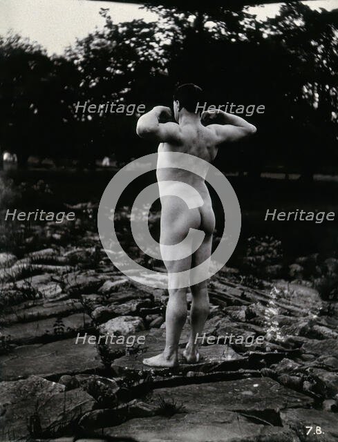 A man posing naked, with his back to the camera, standing on a rocky outcrop, c1900. Creator: Unknown.
