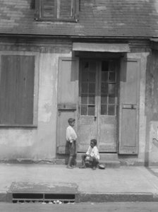Two children outside a door with shutters in the French Quarter, New Orleans, between 1920 and 1926. Creator: Arnold Genthe.