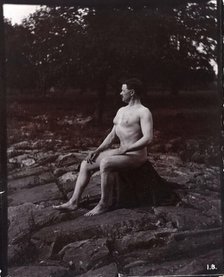 A man posing naked, seated on a rocky outcrop in a leafy landscape, c1900. Creator: Unknown.