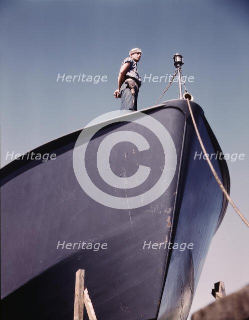 A Coast Guard sentry stands watch over a new torpedo boat under construction at a southern..., 1942. Creator: Howard Hollem.