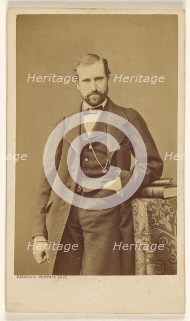 Unidentified well-dressed bearded man standing, elbow on books on a table, 1865-1870. Creator: Bayard & Bertall.