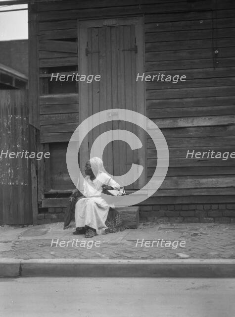 Woman sitting on steps holding a basket, New Orleans, between 1920 and 1926. Creator: Arnold Genthe.
