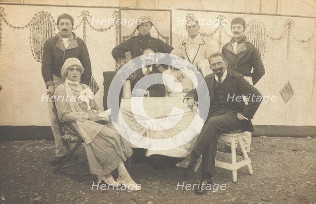 German soldiers, some in drag, pose round a table at a concert party, (between 1910 and 1919?). Creator: Unknown.