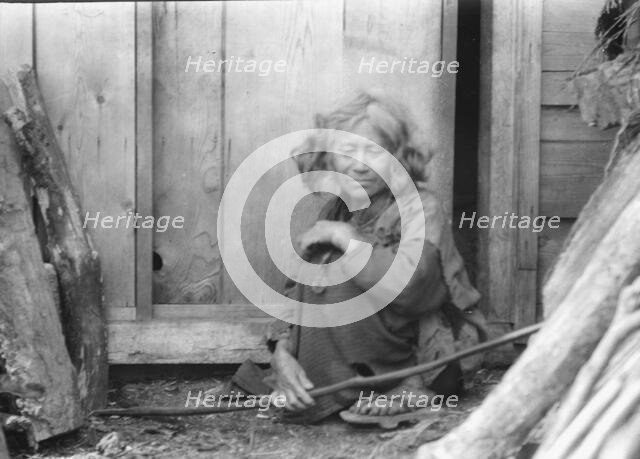 Ainu woman seated by the door of a wooden hut, 1908. Creator: Arnold Genthe.