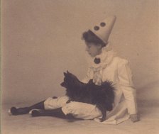 Girl dressed in a pierrot costume with a small black dog on her lap, between 1900 and 1920. Creator: Unknown.