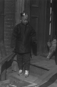 Boy standing on steps in front of a doorway, Chinatown, San Francisco, between 1896 and 1906. Creator: Arnold Genthe.