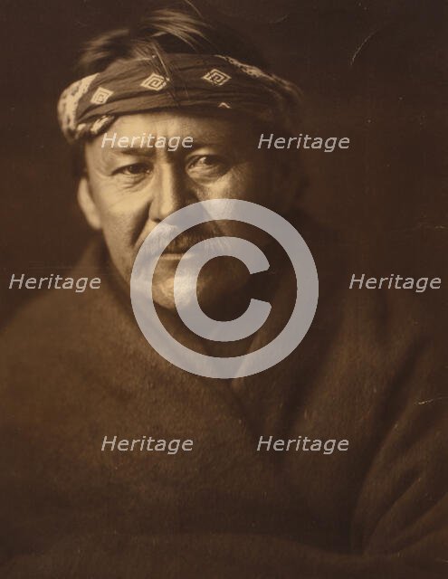 A Navajo man, head-and-shoulders portrait, wearing blanket and headband, facing front, c1904. Creator: Edward Sheriff Curtis.