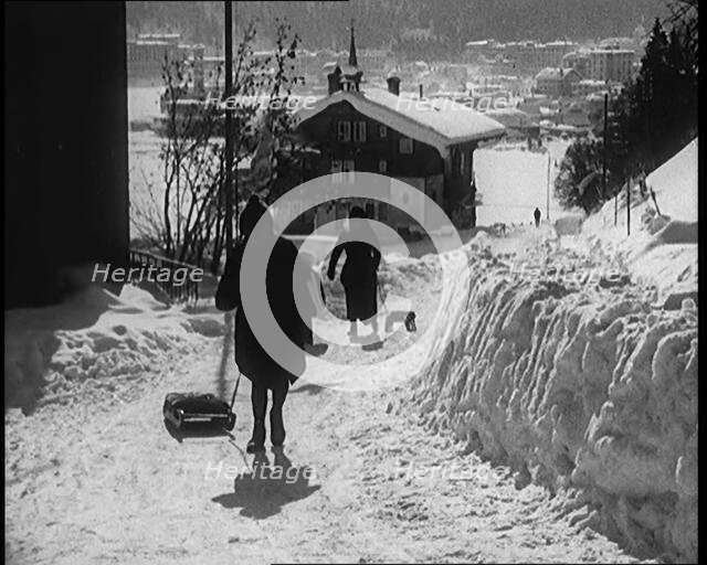 A Group of Female Civilians Skiing down a Snowy Hill with a Picturesque Alpine Village..., 1920. Creator: British Pathe Ltd.