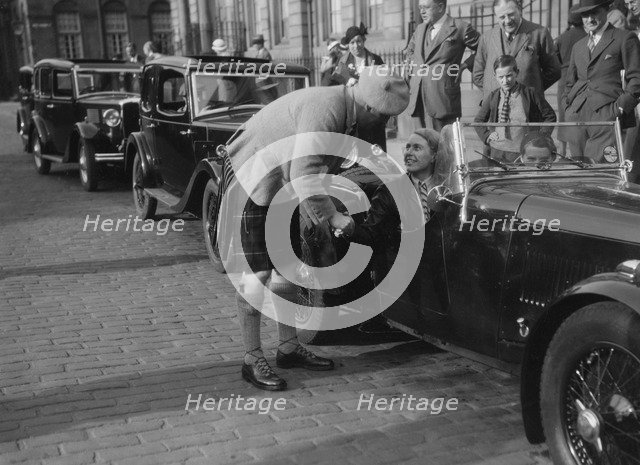 Kitty Brunell in her Aston Martin, chatting to a man in Highland dress, RSAC Scottish Rally, 1933. Artist: Bill Brunell.