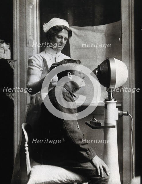 A young uniformed man sitting with a pillow on his chair, facing a machine..., c1910s. Creator: Unknown.