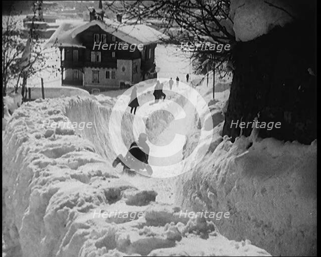 A Female Civilian Sledging down a Snowy Track Watched by Other Civilians with a Picturesque..., 1920 Creator: British Pathe Ltd.