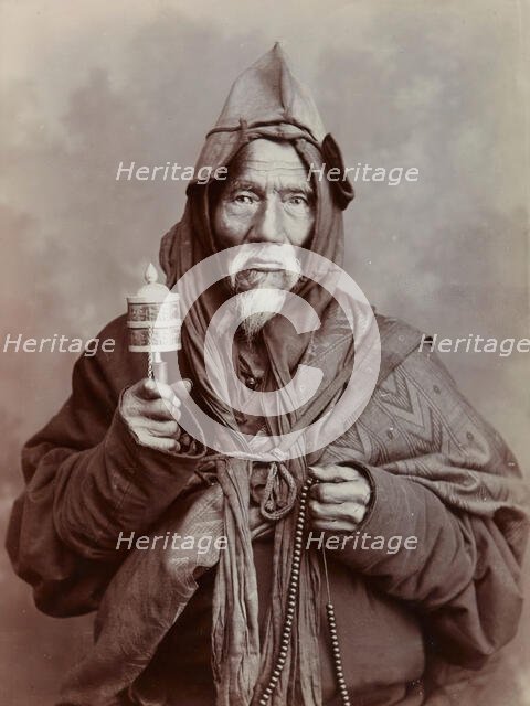 A bearded elderly man, carrying a prayer wheel and a rosary, in a studio setting, c1900. Creator: Thomas Parr.