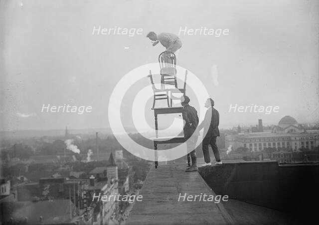 J. Reynolds, Performing Acrobatic And Balancing Acts On High Cornice Above 9th Street, N.W., 1917. Creator: Harris & Ewing.