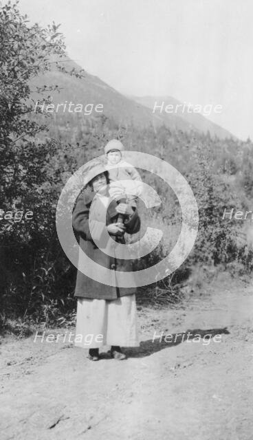 Woman standing on dirt road holding child; mountains in background, between c1900 and 1916. Creator: Unknown.