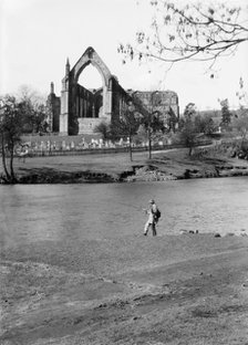 A fisherman on the River Wharfe in front of the ruins of Bolton Priory, North Yorkshire, 1940. Artist: Walter Scott.