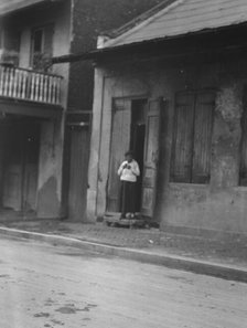 View from across street of a woman standing in a doorway in the French Quarter, New..., c1920-c1926. Creator: Arnold Genthe.