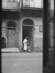 View from across street of a woman cleaning the sidewalk, New Orleans, between 1920 and 1926. Creator: Arnold Genthe.