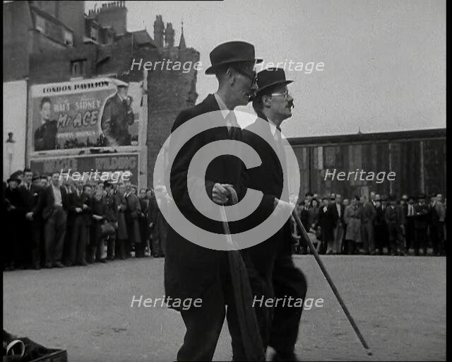 Two British Men in Suits and Hats Dancing in a Square With Men and Woman Watching Them..., 1938. Creator: British Pathe Ltd.