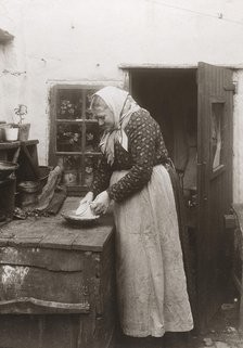 A woman in apron and headscarf washing up a mug outside her home, Landskrona, Sweden, 1910. Artist: Unknown