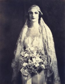 Bride holding a wedding bouquet, facing front, three-quarter length portrait, between 1920 and 1930. Creator: Unknown.