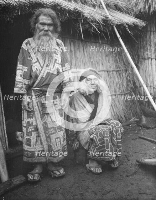 Ainu man and seated woman at the entrance of a hut, 1908. Creator: Arnold Genthe.