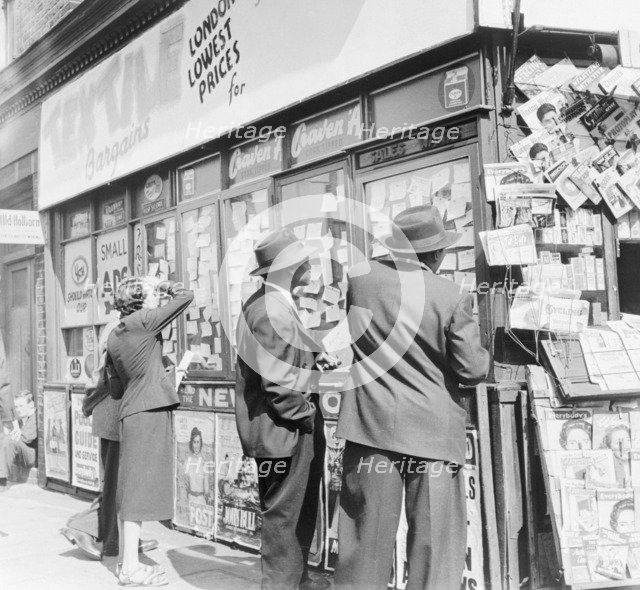 Looking at accomodation notices and job vacancy advertisements in a newsagents window, c1955. Artist: Henry Grant