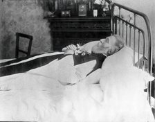 A dead man, wearing robes, lying on his deathbed, (1900?). Creator: Unknown.