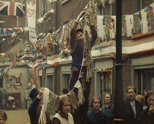 Man Hanging Bunting from a Lamp Post in a Street With Decorations For the Coronation of..., 1937. Creator: British Pathe Ltd.