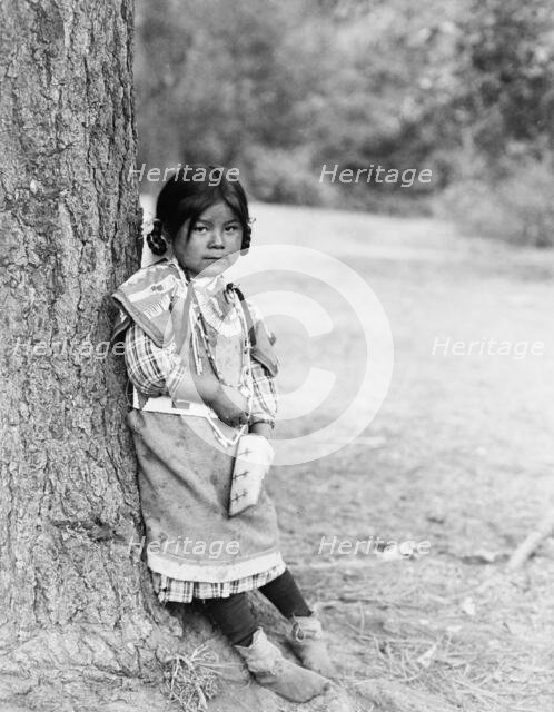 Innocence, an Umatilla girl, full-length portrait, standing by tree, facing slightly right, c1910. Creator: Edward Sheriff Curtis.