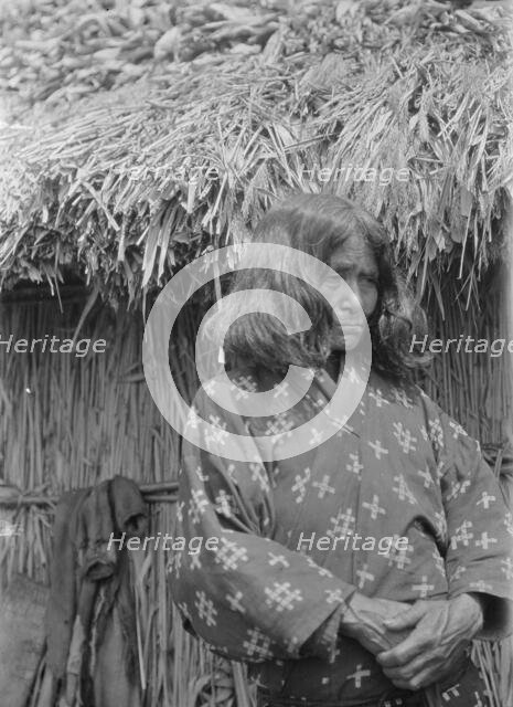 Ainu woman standing outside a hut, 1908. Creator: Arnold Genthe.