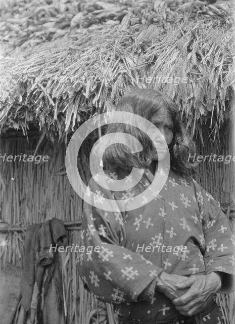 Ainu woman standing outside a hut, 1908. Creator: Arnold Genthe.