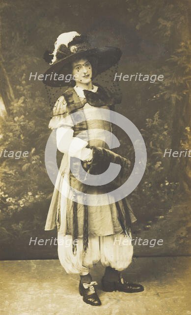 A man in drag wearing a very large hat with a veil, stands in front of a painted..., 1911. Creator: Unknown.