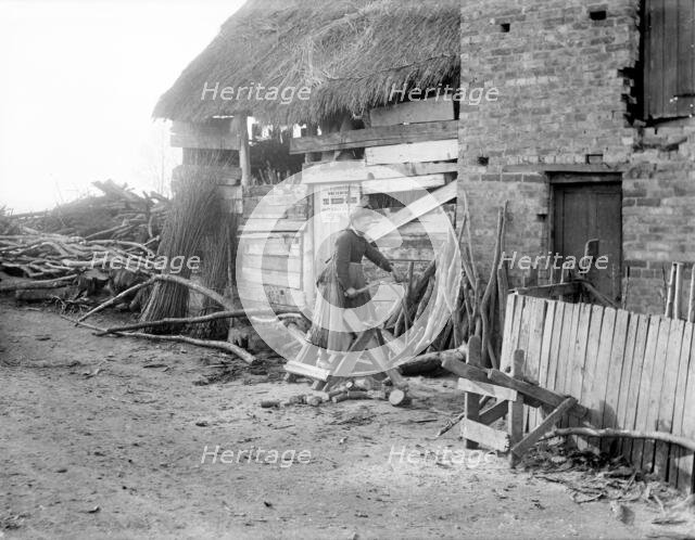 A woman sawing logs outside an outbuilding used as a wood store, Godstow, Oxford, Oxfordshire, 1900. Creator: Henry Taunt.