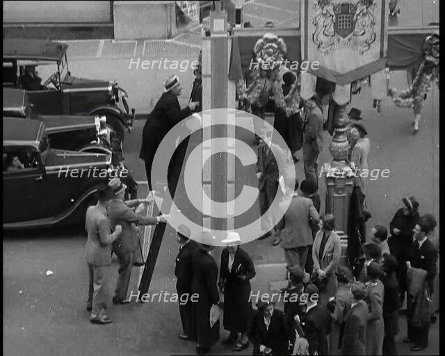 Bud Flanagan With a Frying Pan Climbing a Ladder Resting Against Coronation Decorations in..., 1937. Creator: British Pathe Ltd.