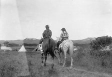 Two daughters of a chief on horseback, riding away from camera toward tents in background, c1907. Creator: Edward Sheriff Curtis.