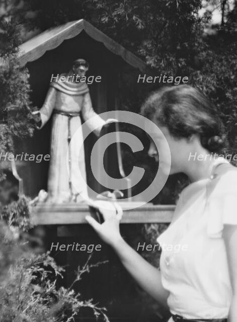 Brady, Victoria, Miss, with a statue of St. Francis in a garden, 1931 July 14. Creator: Arnold Genthe.