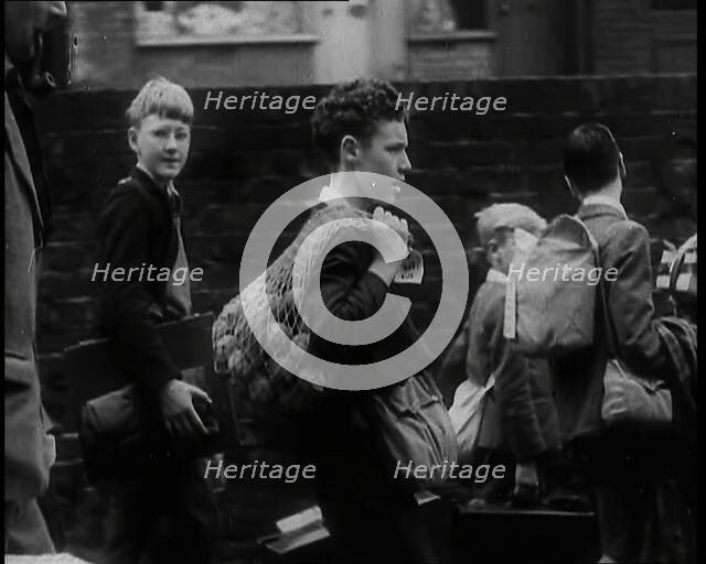 A Small Group of British Male Evacuees Carrying Bags and Walking Next to a Brick Wall, 1939. Creator: British Pathe Ltd.