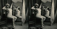 A woman posing naked in a photographic studio, sitting on a chair in front of a looking-glass, c1900 Creator: Unknown.