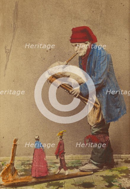 Unidentified man in cap playing a bagpipe-type instrument with two marionettes, about 1870. Creator: Giorgio Conrad.