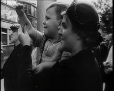 A British Woman Holding up a Young Boy Who is Waving in the Direction of a Bus as Other..., 1939. Creator: British Pathe Ltd.