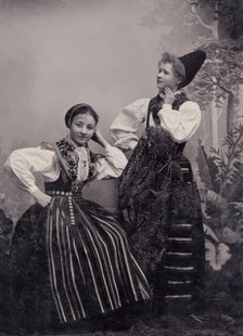 Studio portrait of two young girls posing in folk costumes from Dalarna, 1880-1907. Creator: Helene Edlund.