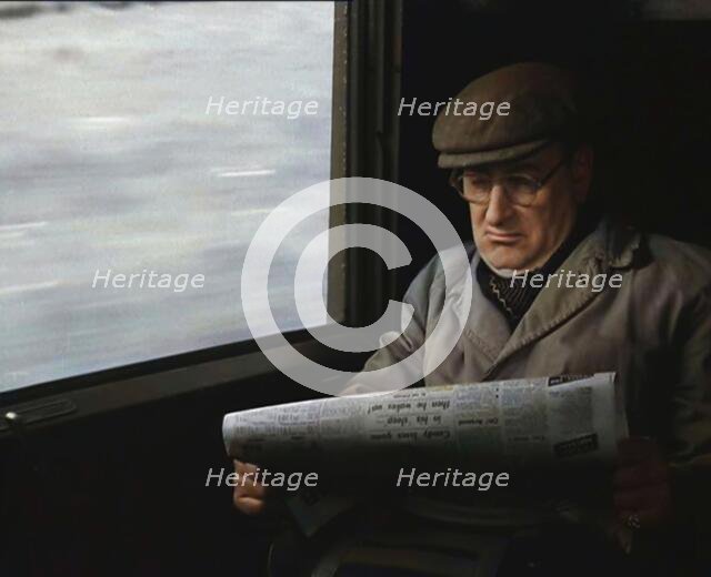 A Man in a Flat Cap and Spectacles Reading a Folded Newspaper in the Window Seat of a Train..., 1938 Creator: British Pathe Ltd.