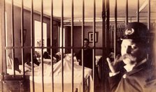 Bellevue Hospital, New York City: male patients (criminal insane?) in bed in ward, prison bars in... Creator: Unknown.