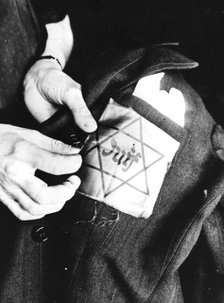 Sewing the yellow star identifying a Jew onto a jacket, German-occupied Paris, 1942. Artist: Unknown