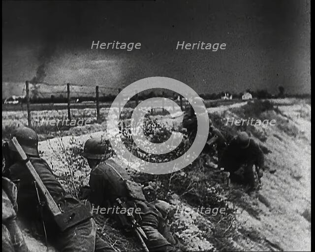 Four Male German Army Soldiers Lying Low on a Slope Below a Fence While Columns of Smoke..., 1939. Creator: British Pathe Ltd.