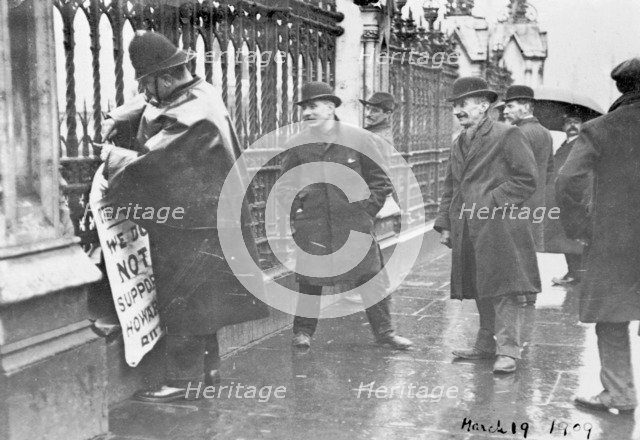 A policeman removes a suffragette poster from the railings, House of Commons, London, March 1909. Artist: Unknown