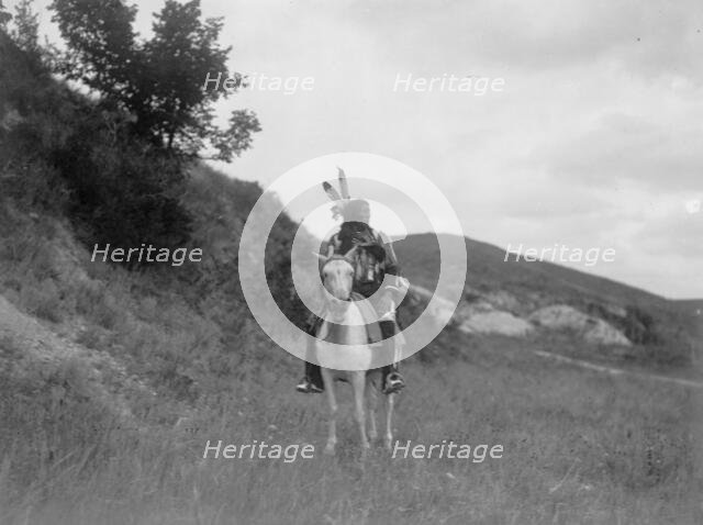 Sioux Indian on horseback, wearing two feathers, beaded buckskin shirt, and leggings..., c1907. Creator: Edward Sheriff Curtis.
