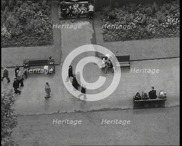 An Overhead Shot of Pedestrians Walking up and Down a Path or Sitting on Benches in a Park..., 1938. Creator: British Pathe Ltd.